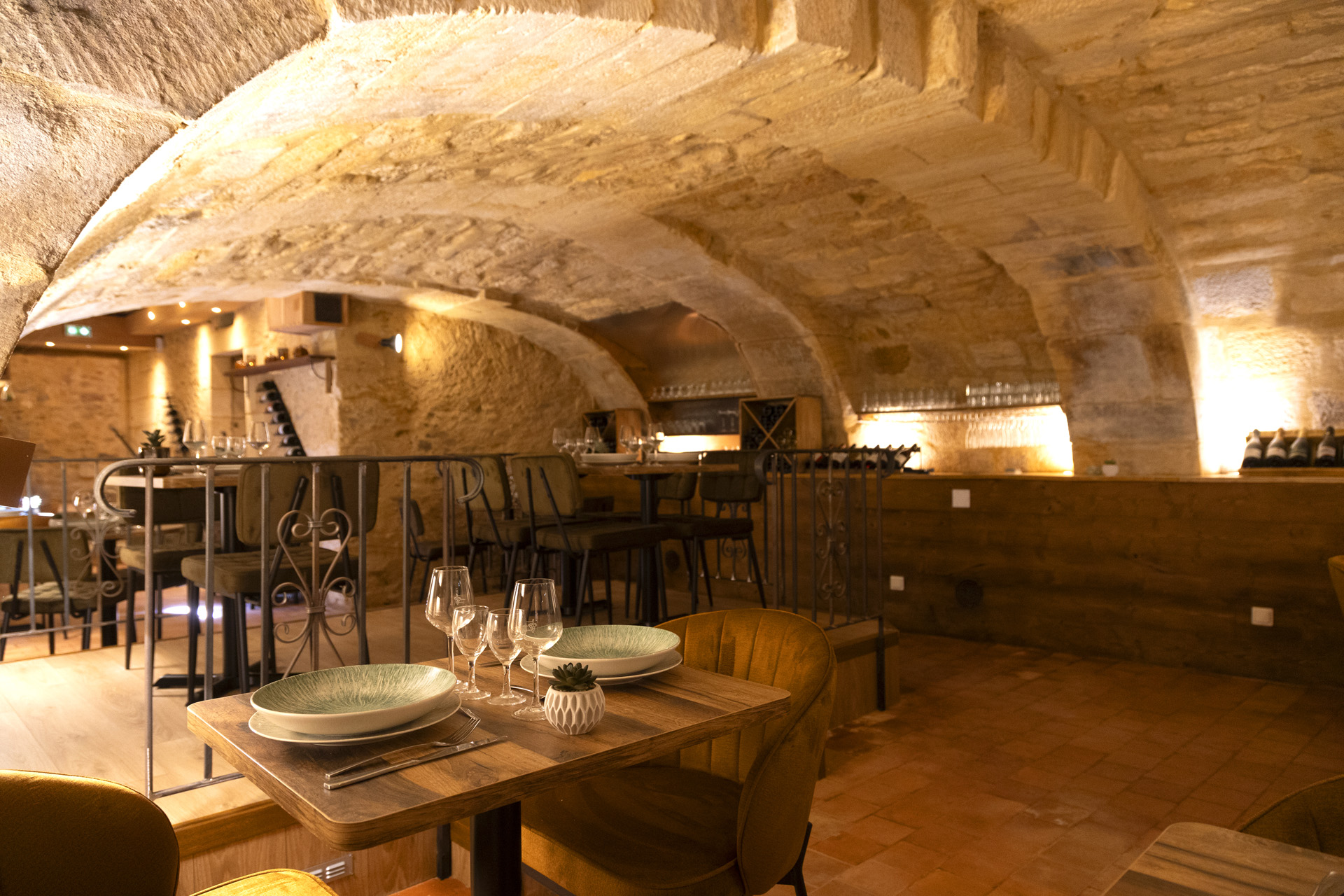 Salle du restaurant Arcadia sous les voûtes de pierre, fauteuils moutarde et tables en bois