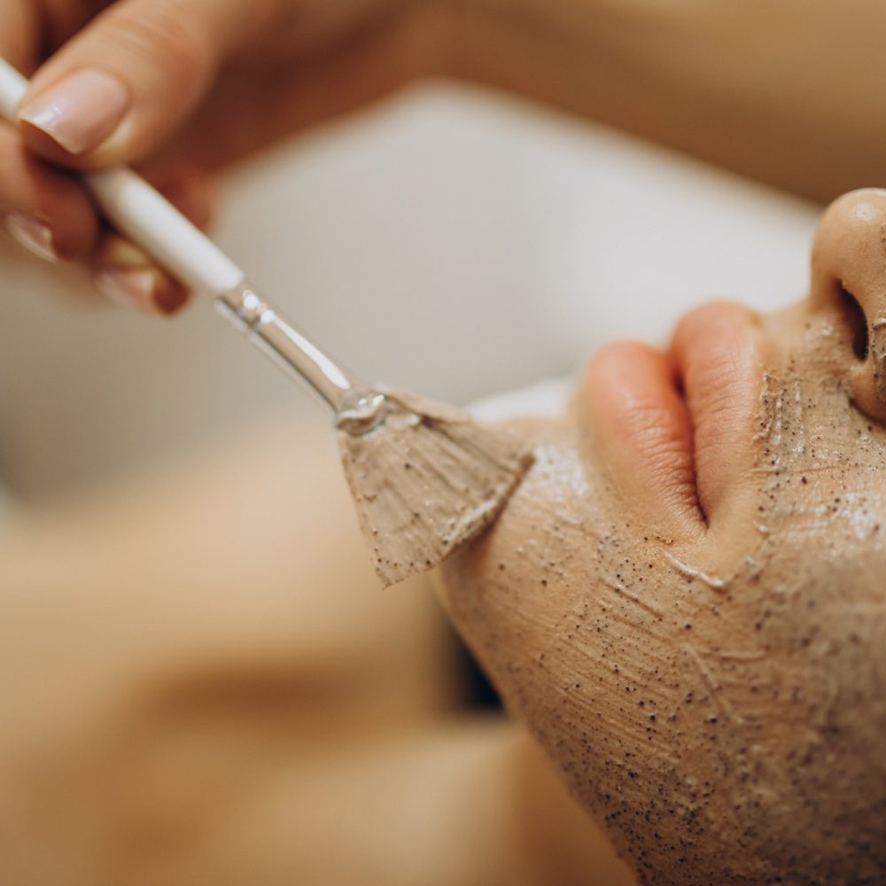 Esthéticienne appliquant au pinceau un masque sur le visage d'une cliente