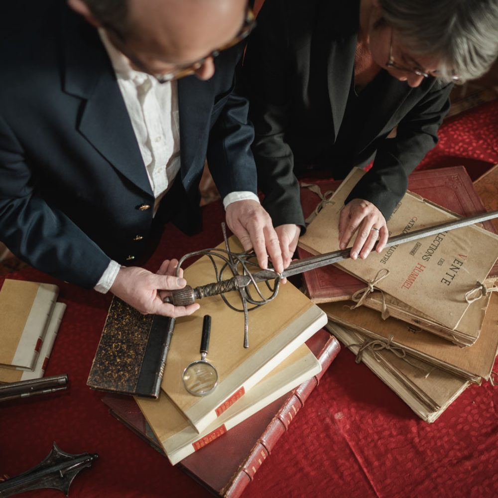 Deux experts examinant une épée et des livres anciens, loupe en main