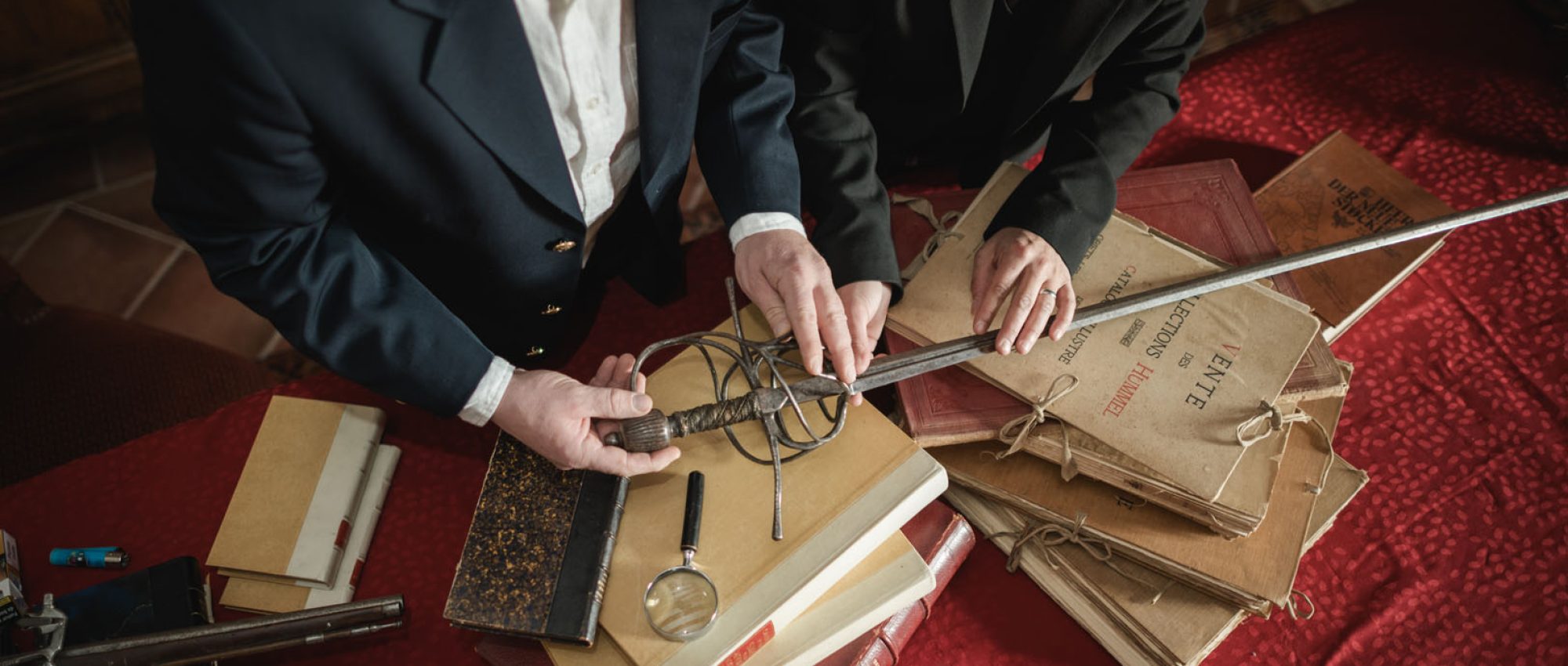 Deux experts examinant une épée et des livres anciens, loupe en main