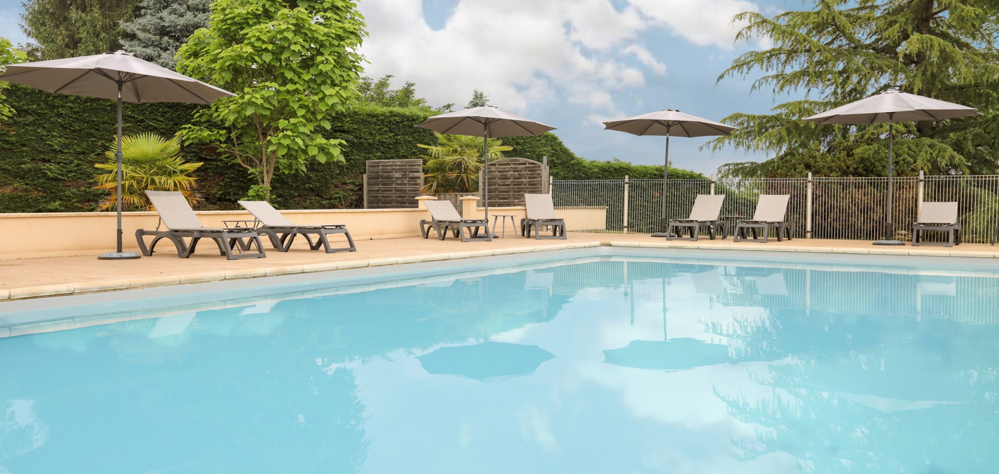 Piscine extérieure de l’hôtel Le Mas del Pechs à Sarlat, transats et parasols sous les arbres