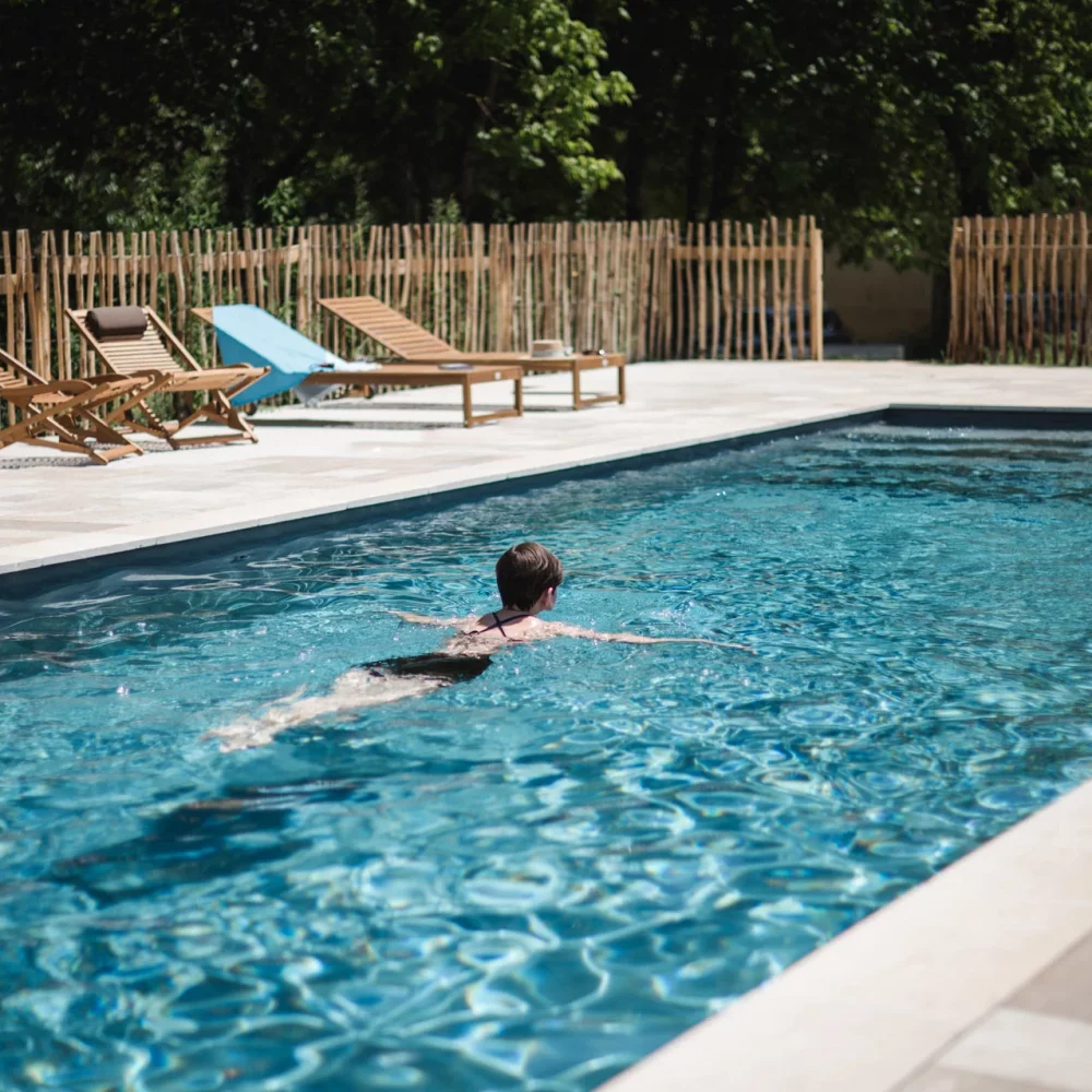 Nageuse dans une piscine extérieure bordée de transats et d'une clôture en châtaignier