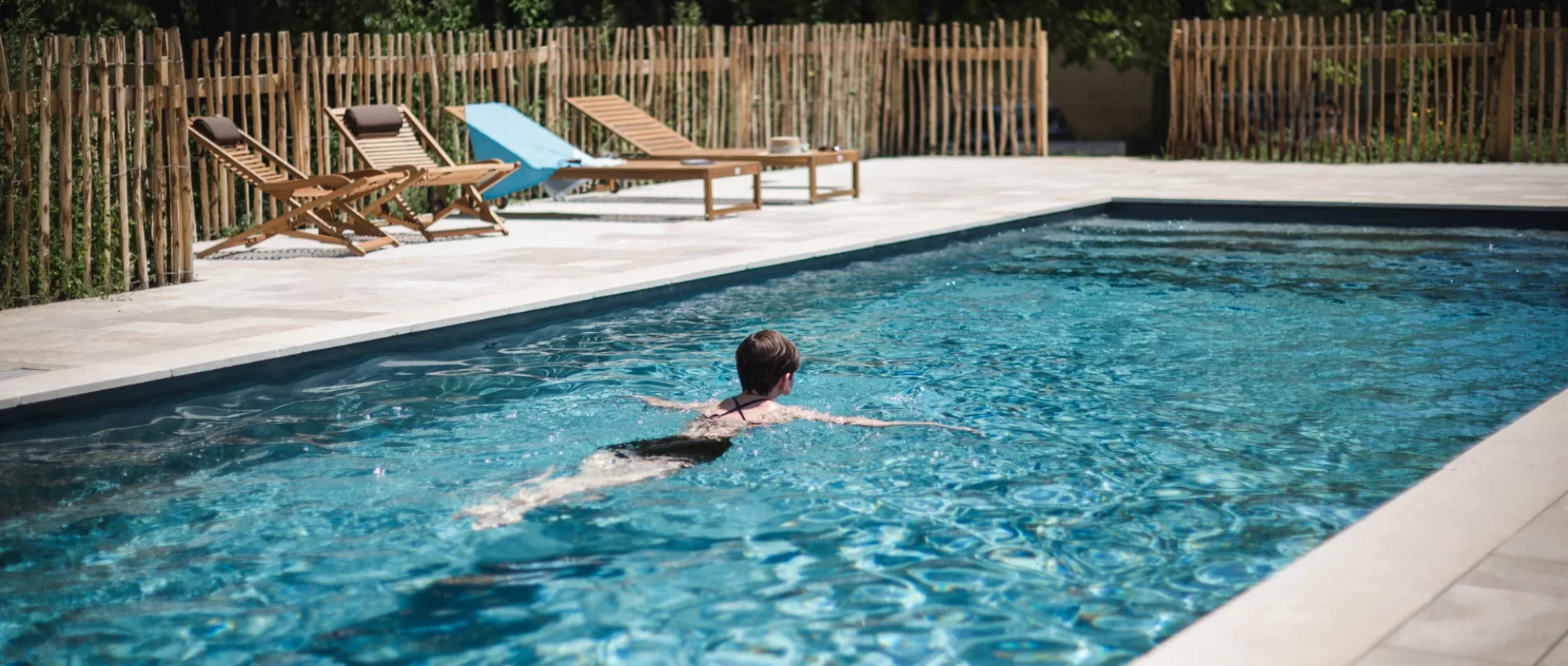Nageuse dans une piscine extérieure bordée de transats et d'une clôture en châtaignier