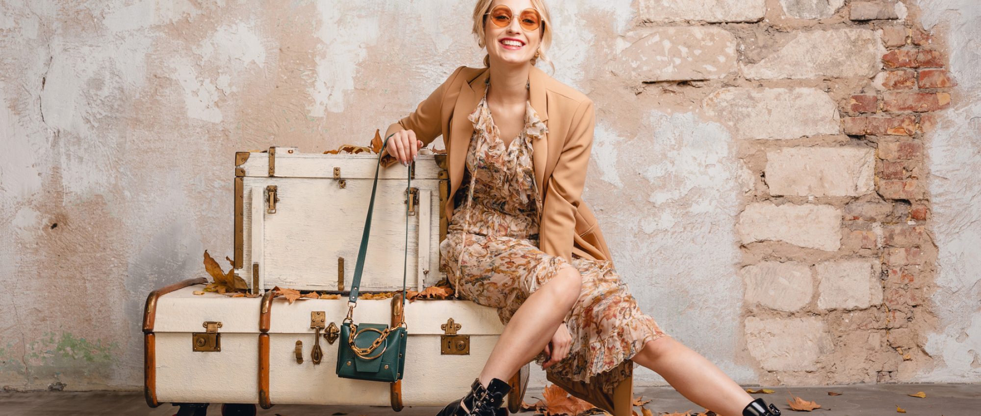 Femme en tenue d'automne assise sur des malles vintage devant un mur en pierre