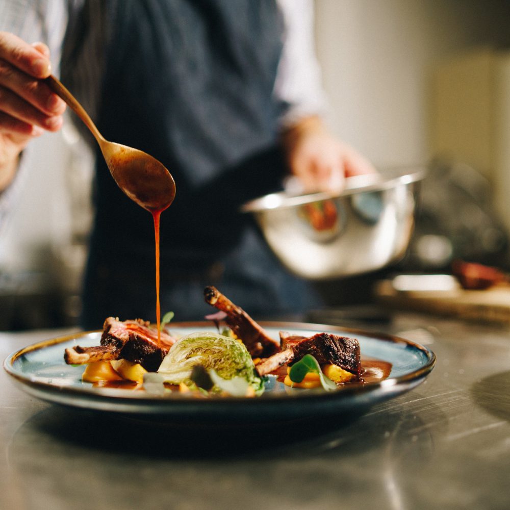 Chef nappant de sauce une assiette de viande et de légumes en cuisine