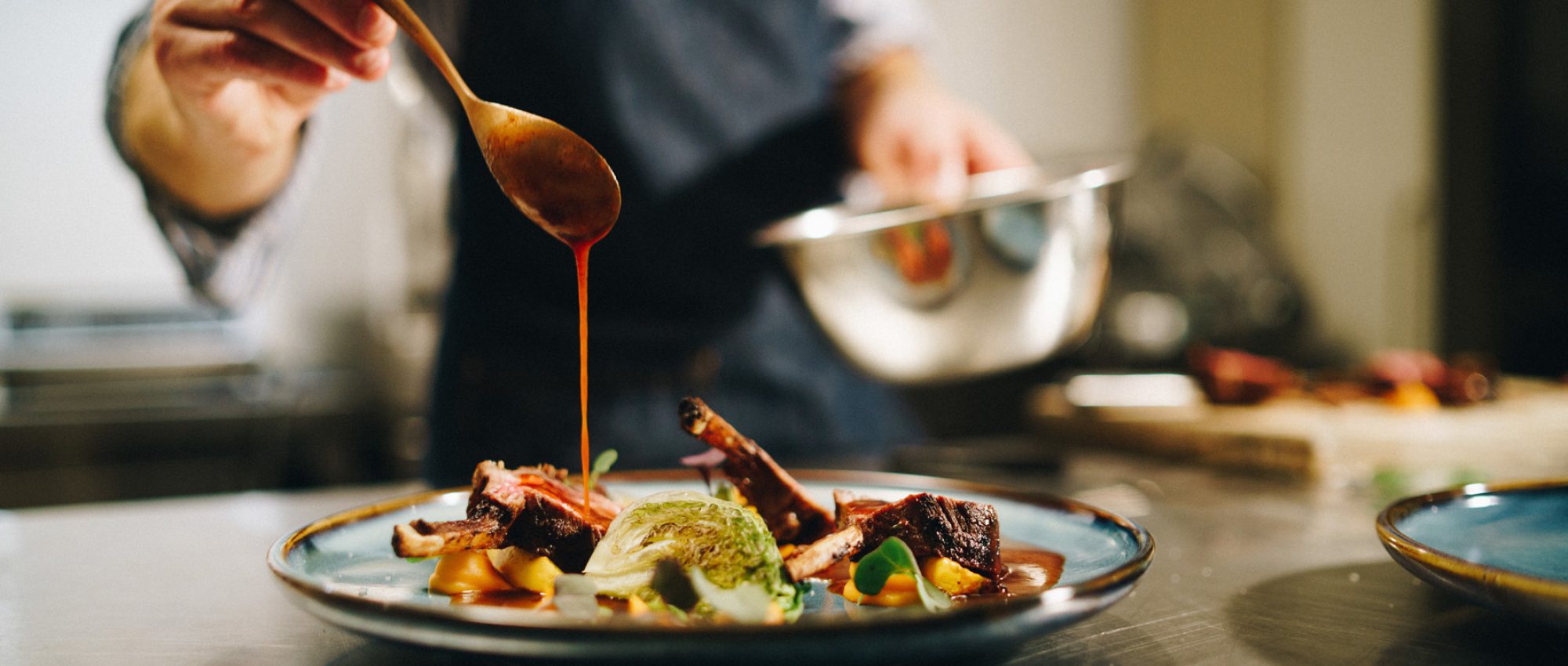 Chef nappant de sauce une assiette de viande et de légumes en cuisine